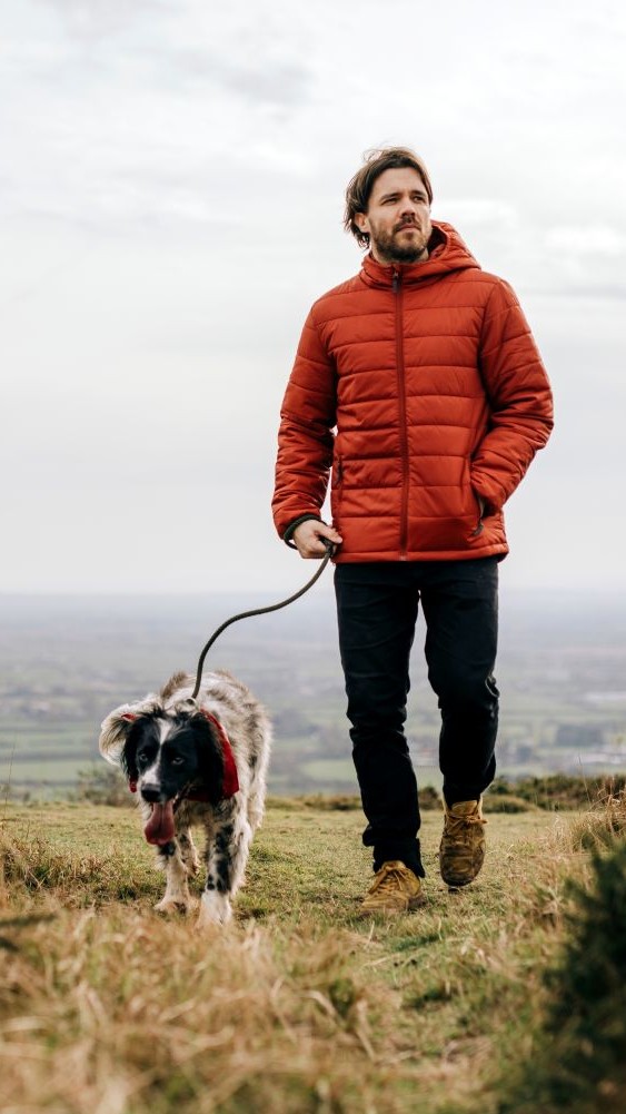 image shows a man walking a dog on a grassy hill.
