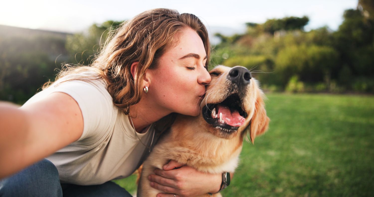 image shows a woman sharing an affectionate moment by kissing her Golden Retriever